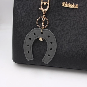 Detail of grey horseshoe PU leather bag charm with gold hardware on a black tote bag