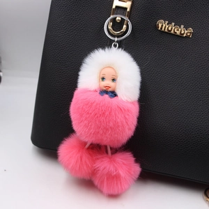 Close-up of pink plush sleeping doll pendant hanging on a black textured handbag
