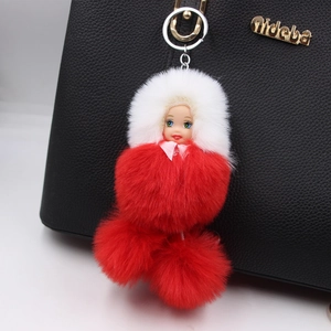 Detail of red and white sleeping doll pom-pom pendant hanging on a black leather handbag