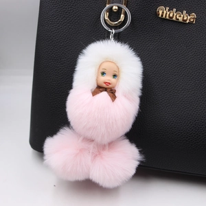 Pink and white fluffy doll keychain accessory hanging on a black leather handbag