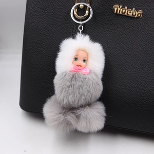 Cute sleeping doll pom pom keychain hanging on a black textured leather handbag