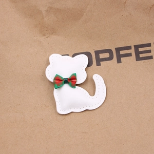 Detalle del colgante de gato de cuero blanco con lazo de cuadros rojos y verdes sobre papel