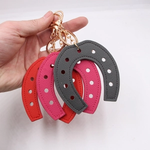Three horseshoe-shaped leather keychains in red, pink, and grey with gold-tone hardware