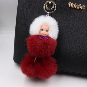 Close-up of a plush sleeping doll keychain with soft fur balls on a black leather bag
