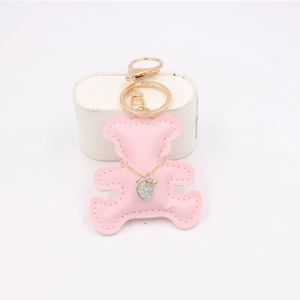 Detail of a pink leather bear keychain with gold clasp and engraved silver charm pendant