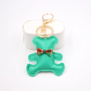 Detailed view of green leather bear charm with a red-green plaid bow and golden metal clasp
