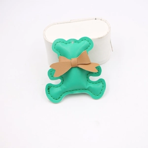 Detailed view of handmade green leather bear pendant with fine stitching and brown bow charm