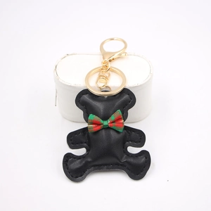 Close-up of black leather bear keychain with red-green plaid bow and golden metal clasp