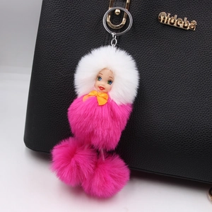 Detail of cute sleeping doll plush keychain with white and rose pink fur balls on black bag
