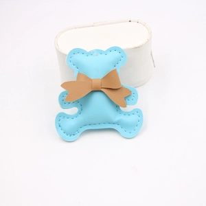 Detail view of light blue leather bear charm with brown bow and white stitching