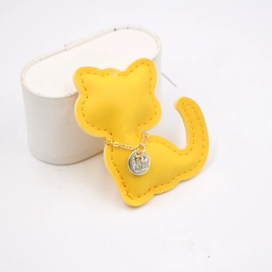 Macro detail of a bright yellow leather cat charm with fine stitching and silver chain