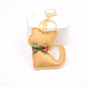Dettaglio portachiavi a forma di gatto in pelle color cammello con fiocco scozzese rosso