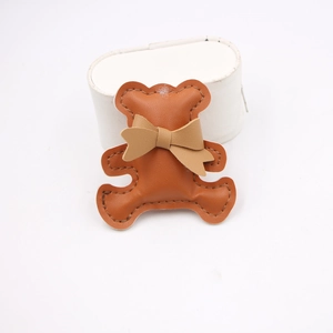 Detail of brown faux leather bear charm featuring stitched edges and a cute bow tie