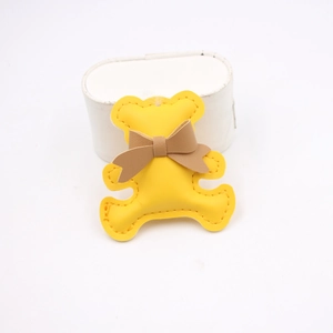 Detailed close-up of a bright yellow leather bear charm with a khaki bow and hand-stitched edges