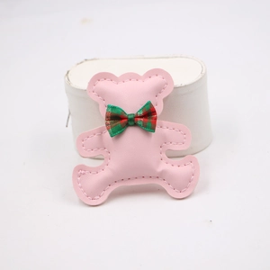 Detailed view of a pink faux leather bear charm with fine white stitching and a plaid bow