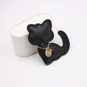 Detailed view of a black leather cat charm with a gold chain and a round metal logo tag