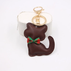 Dettaglio portachiavi a gatto in pelle marrone con fiocco scozzese rosso e gancio oro