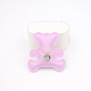 Detail showing a gold chain necklace with embossed pendant on a pink bear-shaped leather plate