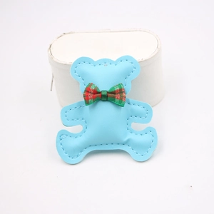 Close-up of a light blue leather bear charm with a red and green plaid bow tie detail