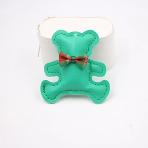Detail of green leather bear phone charm with red-green plaid bow on white stand