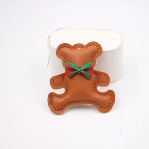 Detailed view of a brown teddy bear leather charm with a red and green plaid bow tie