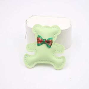 Detail of light green bear leather phone charm with a plaid bow and white stitching detail
