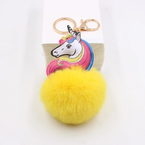 Detail of yellow plush pompom keychain with printed unicorn leather charm and gold clasp