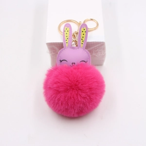 Close-up of a pink plush pompom keychain with purple rabbit ears and golden metal clasp