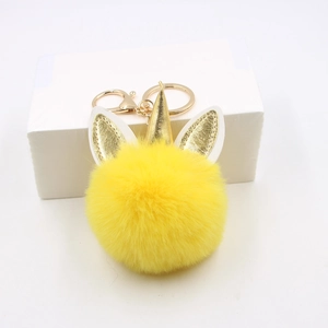 Gros plan du porte-clés licorne en peluche jaune avec corne dorée sur boîte cadeau