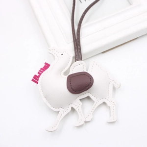 Detail of a white PU leather camel keychain with pink tassels and brown saddle decor
