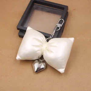 Detailed close-up of cream white faux leather bow pendant with silver metal heart charm