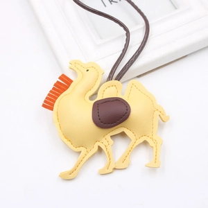 Detailed view of yellow PU leather desert camel bag charm with brown saddle and orange tassels