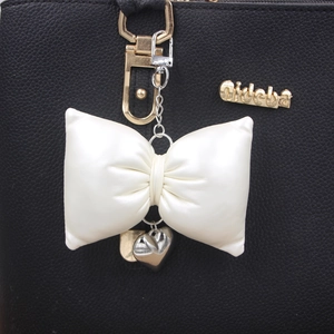 Elegant cream butterfly bow bag charm with a small silver heart pendant on black leather