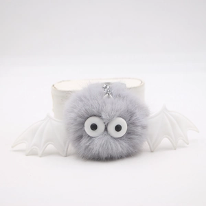 Detail of grey plush monster keychain with white bat wings and silver metal chain