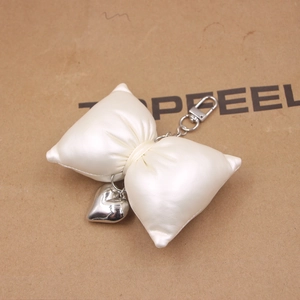 Detail view of a cream bow keychain with heart pendant and silver lobster clasp accessory