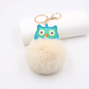 Détail du pendentif hibou en simili cuir bleu avec pompon beige et porte-clés doré