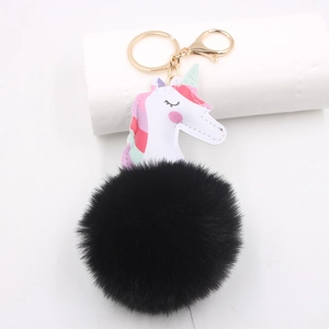 Detail of white leather unicorn charm with colorful mane on a large black fluffy pompom