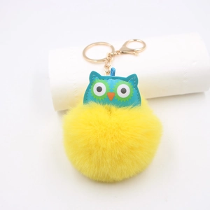 Détail macro du porte-clés hibou en peluche avec pompon jaune et fermoir mousqueton doré