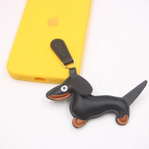 Dettaglio di ciondolo bassotto in pelle PU con anello metallico e smartphone giallo