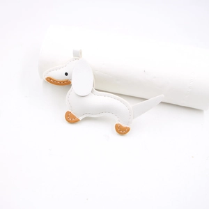 Close-up of white leather dachshund charm with brown stitching and metal hanging loop