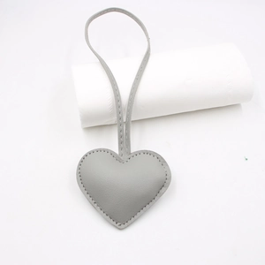 Detail of grey heart leather bag charm with knot strap and visible stitching on white base