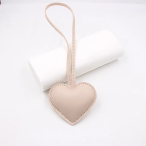 Close-up of heart-shaped leather bag charm with fine stitching and long strap