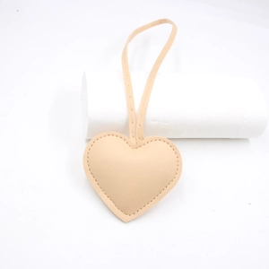 Close-up of beige heart-shaped leather bag charm with litchi grain and hanging strap