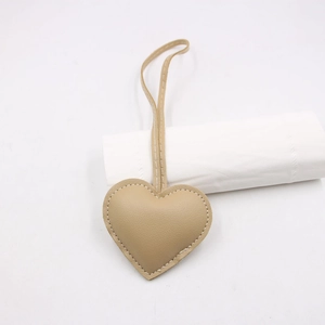 Close-up of khaki heart-shaped leather bag charm with litchi texture and white stitching