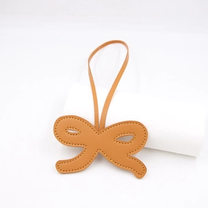 Creative tan leather bow charm with yellow contrast stitching and matching hanging strap
