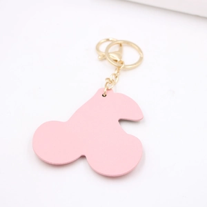 Pink leather cherry keychain with gold clasp and metal ring on white background