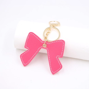 Pink PU leather bow keychain with white stitching and gold lobster clasp on white stand