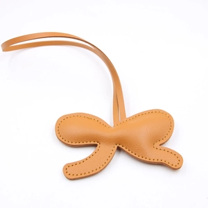 Detail of caramel leather bow charm with yellow contrast stitching and long lanyard cord