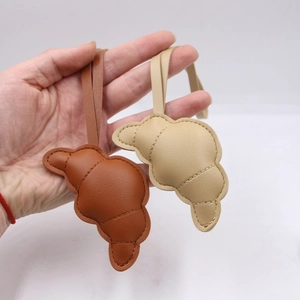 Dettaglio dei ciondoli in pelle a forma di croissant con cuciture fini in caramello e beige