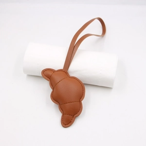 Dettaglio del ciondolo a forma di croissant in pelle caramello con cuciture a vista